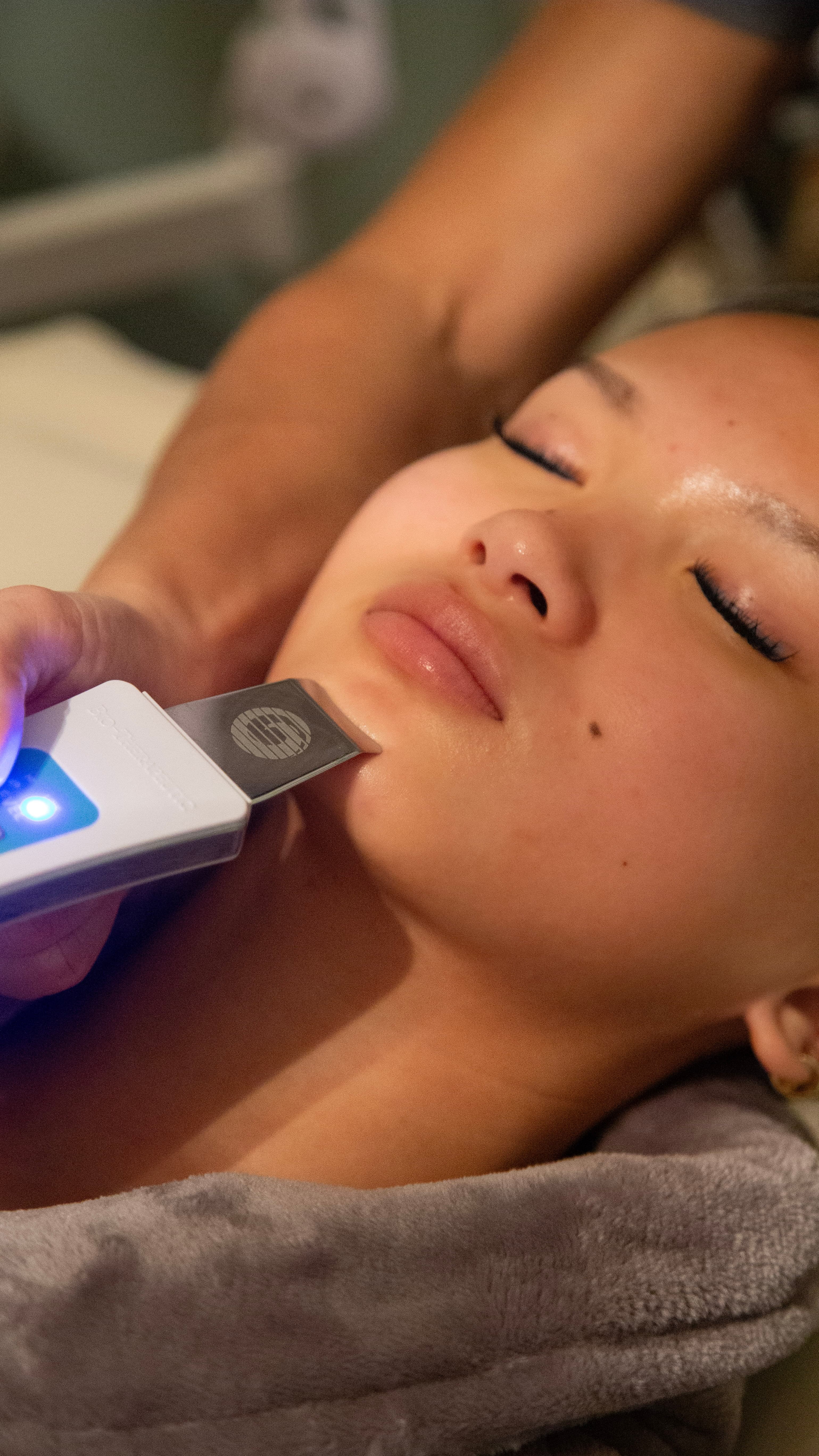 An ultrasonic skin spatula gliding across a client's cheek during a facial